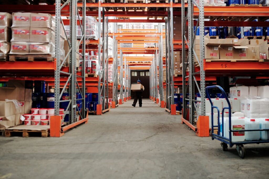 pexels-photo-4483774 A worker carrying a box in a well-organized warehouse storage aisle.